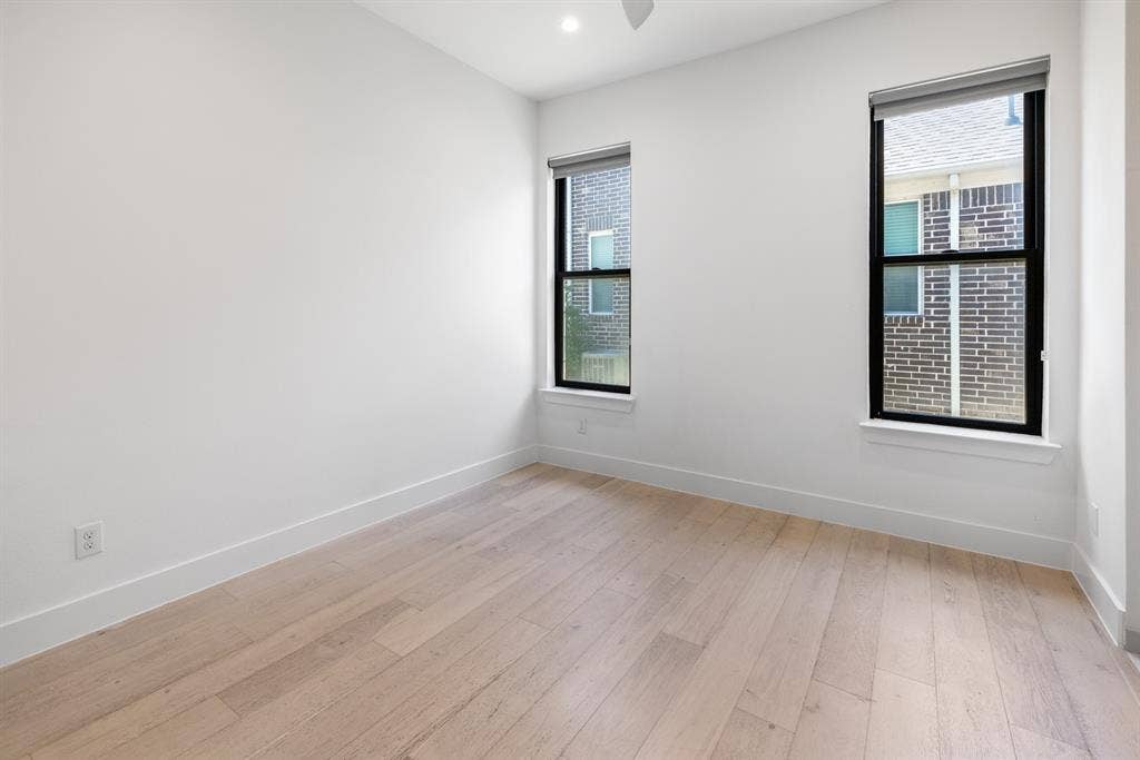 1321 Black Walnut Lane, Arlington, TX 76005 Bright corner bedroom featuring two large double-hung windows with black frames, light wood-finish flooring, and clean white walls with neutral trim