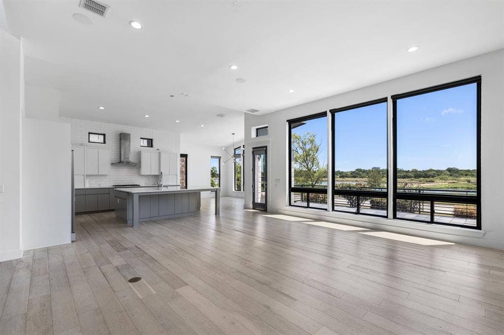 1321 Black Walnut Lane, Arlington, TX 76005 Open-concept living space featuring wide-plank wood-finish flooring, recessed ceiling lighting, and expansive multi-panel glass doors and windows framing pastoral landscape scenery