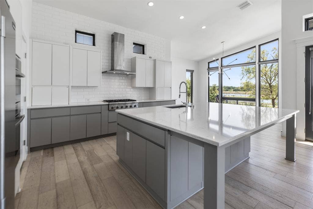 1321 Black Walnut Lane, Arlington, TX 76005 Modern kitchen featuring white upper cabinetry and charcoal lower cabinetry with a large waterfall-edge island, stainless steel range hood, and professional-grade gas cooktop
