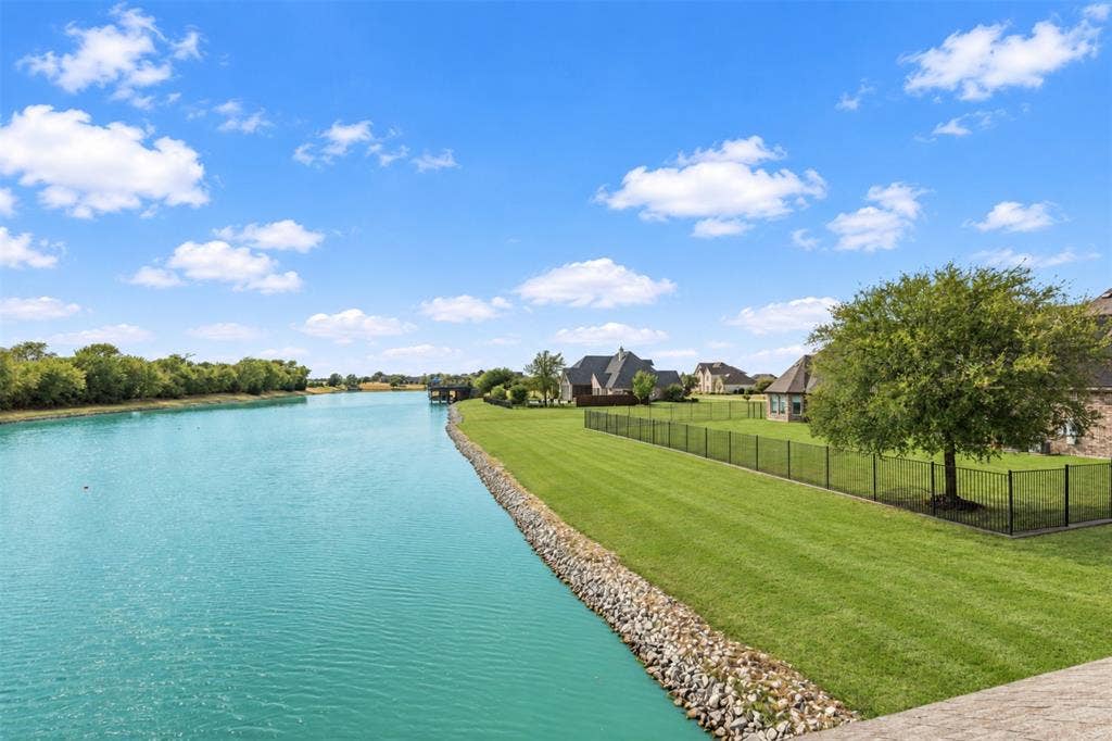 623 Calm Water Cove, Princeton, TX 75407 Waterfront property featuring a black metal fence, extensive green lawn, and mature trees