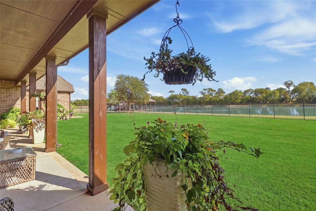 623 Calm Water Cove, Princeton, TX 75407 Covered patio with wood-finish support columns, brick exterior, expansive lawn, black metal fencing, and water feature beyond