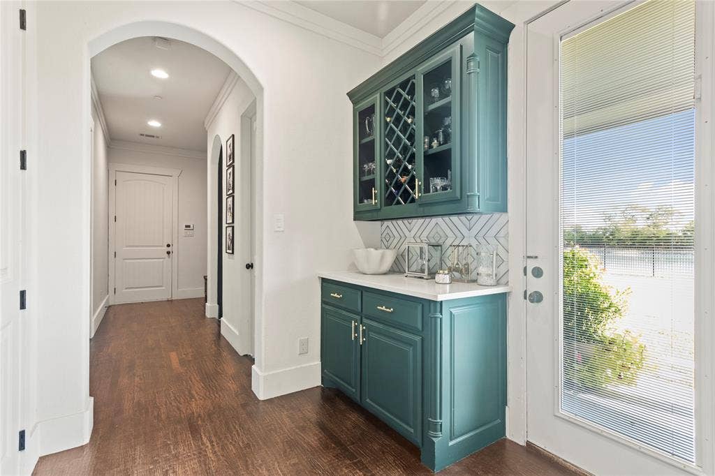 623 Calm Water Cove, Princeton, TX 75407 Built-in cabinetry with glass-front uppers and wine storage, white countertop, patterned tile backsplash, wood-finish flooring, and an arched hallway entry