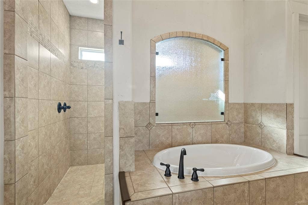 623 Calm Water Cove, Princeton, TX 75407 Tiled shower with a transom window, an arched frosted glass partition, a built-in soaking tub, and oil-rubbed bronze fixtures