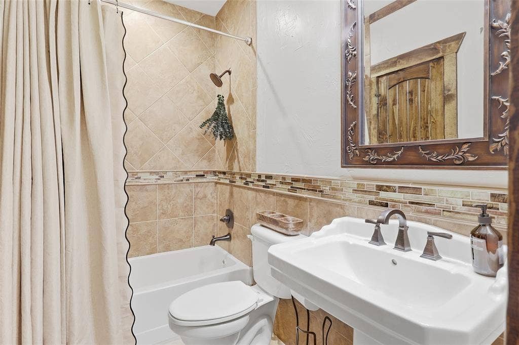 623 Calm Water Cove, Princeton, TX 75407 Pedestal sink with bronze-finish faucet, framed mirror, tiled wainscoting with mosaic accent, and a shower-over-tub with tiled surround