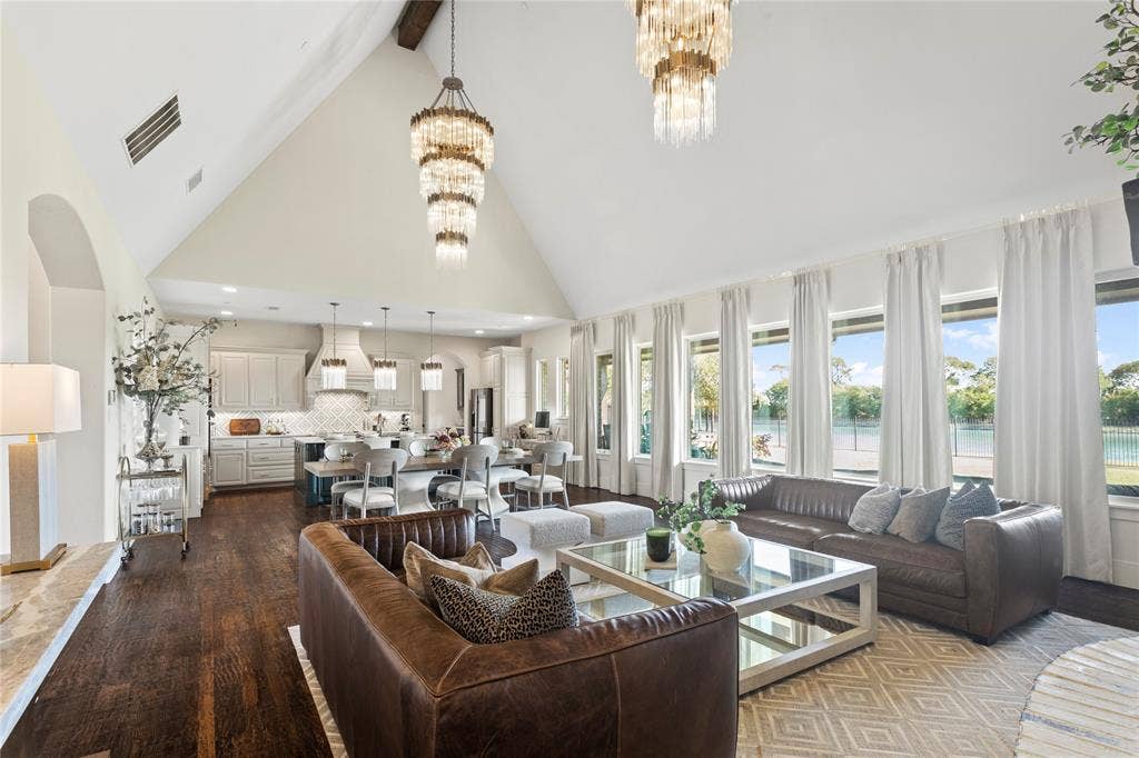 623 Calm Water Cove, Princeton, TX 75407 Vaulted ceilings, wood-finish flooring, multiple tiered chandeliers, a full wall of windows, and built-in kitchen cabinetry