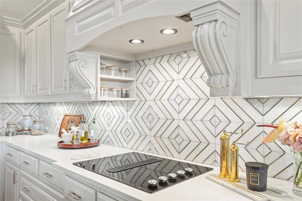 623 Calm Water Cove, Princeton, TX 75407 White cabinetry with chrome hardware, an integrated cooktop with downdraft ventilation, geometric pattern backsplash, recessed lighting, and solid surface countertops