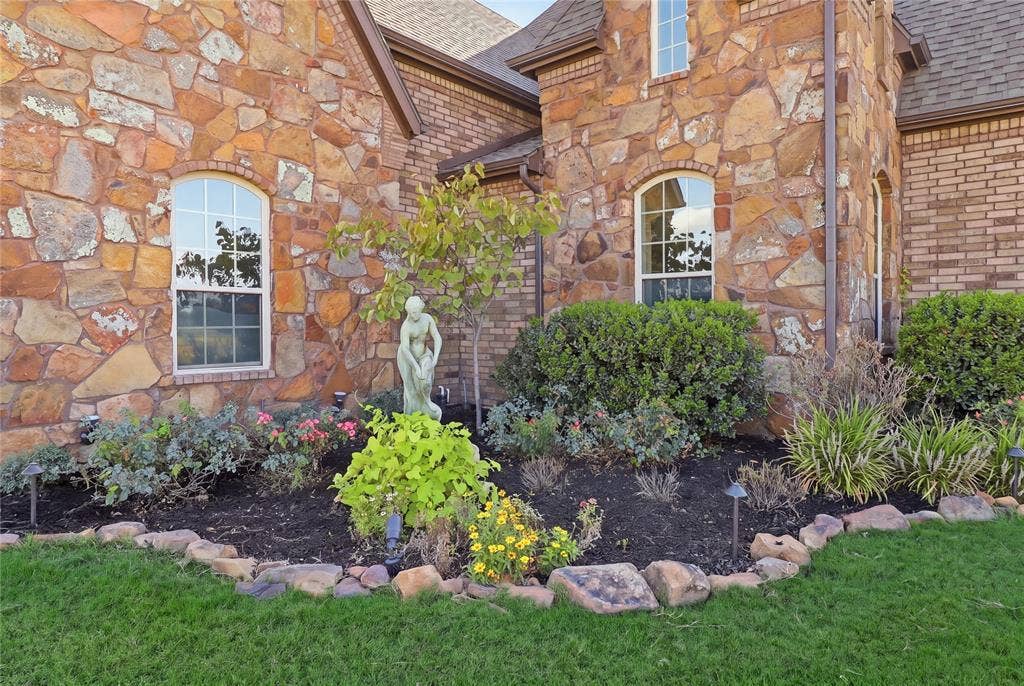 623 Calm Water Cove, Princeton, TX 75407 Stone and brick exterior with arched windows, manicured landscaping, and a stone-edged garden bed