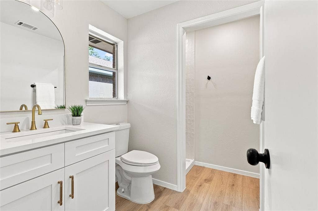 2411 Aspen Street, Richardson, TX 75082 White vanity with gold-finish fixtures and hardware, rectangular undermount sink, and a framed arched mirror