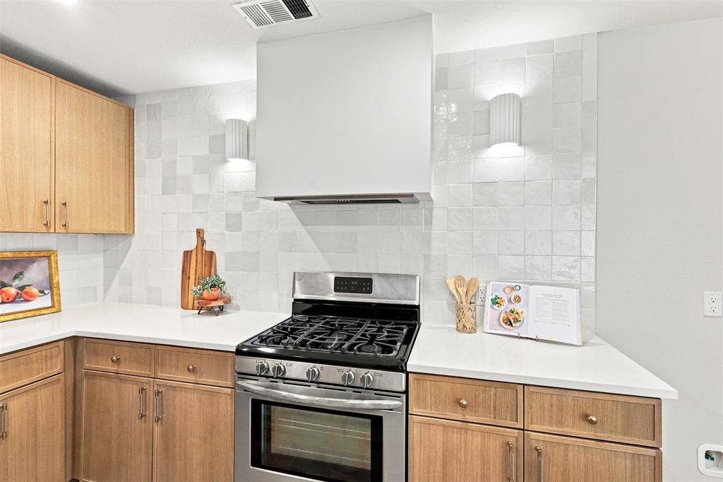 2411 Aspen Street, Richardson, TX 75082 Modern kitchen featuring warm wood-finish cabinetry, white subway tile backsplash, stainless steel gas range with convection oven, and white quartz countertops with ample workspace and storage throughout