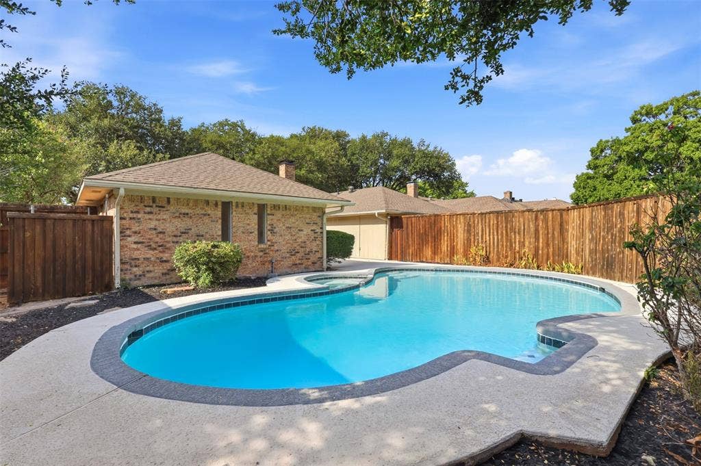 2411 Aspen Street, Richardson, TX 75082 Freeform swimming pool with a concrete surround, wood privacy fencing, and brick exterior structures