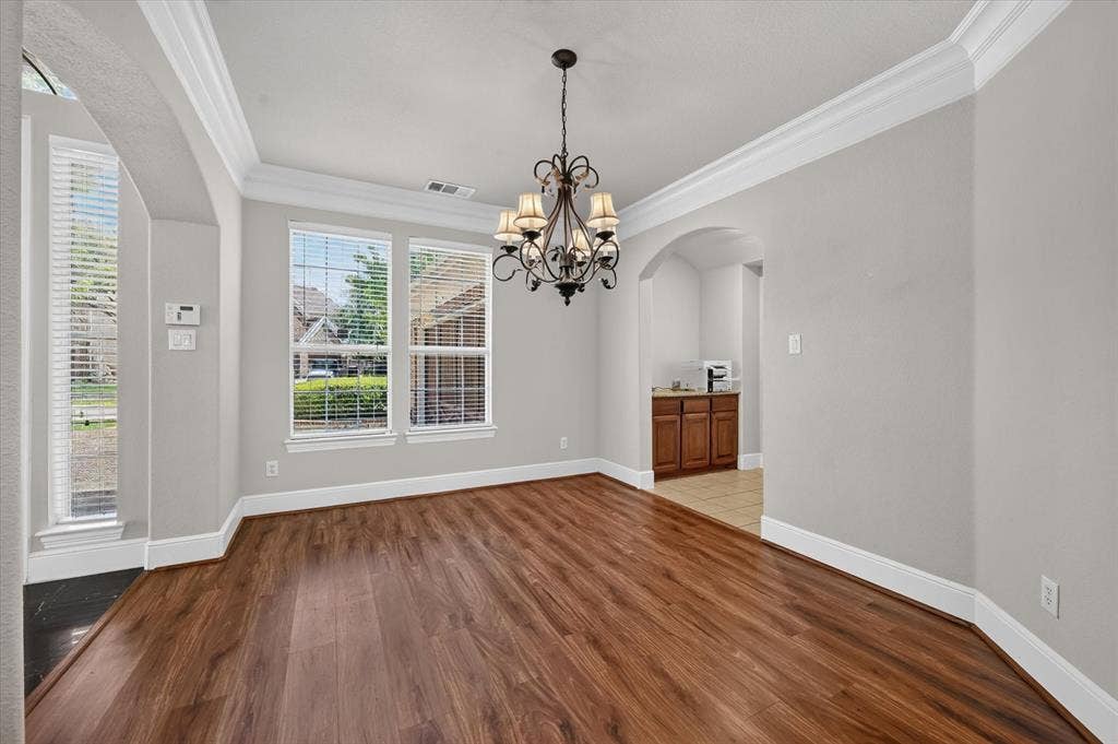 4612 Quiet Circle, Plano, TX 75024 Wood-finish flooring, crown molding, archway, and an ornate chandelier