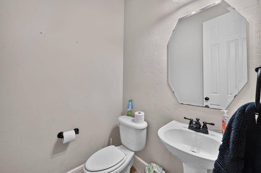 4612 Quiet Circle, Plano, TX 75024 Pedestal sink with dark-finished faucet, rectangular beveled mirror, and textured wall finish