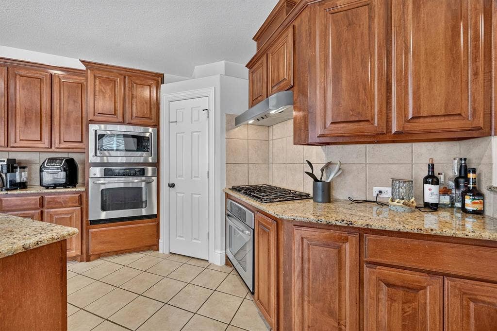 4612 Quiet Circle, Plano, TX 75024 Kitchen featuring extensive wood cabinetry, granite countertops, tile flooring, stainless steel built-in appliances, and a gas cooktop