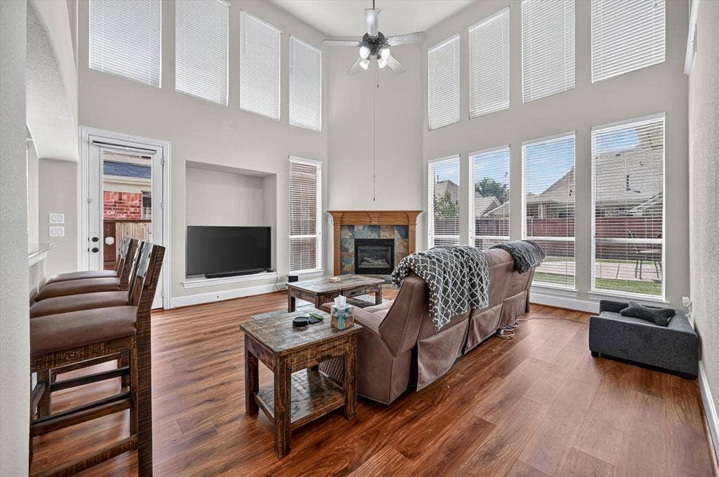 4612 Quiet Circle, Plano, TX 75024 Two-story living area with wood-finish flooring, a stone-surround fireplace, built-in media niche, and multiple windows