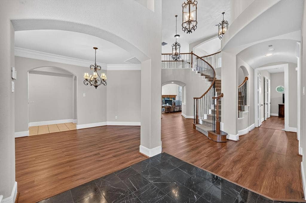 4612 Quiet Circle, Plano, TX 75024 Grand entry with black marble flooring, wood-finish flooring, a winding staircase with dark wood handrails, and elegant chandeliers