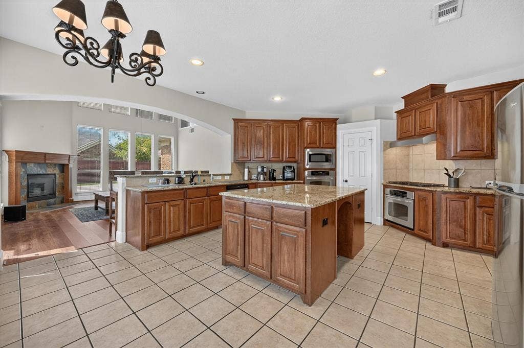 4612 Quiet Circle, Plano, TX 75024 Kitchen featuring wood-finish cabinetry, granite countertops, a central island, stainless steel appliances, and tile flooring