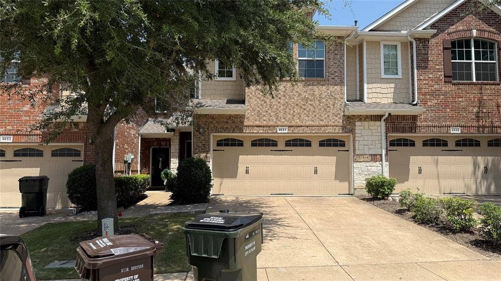 4651 Penelope Lane, Plano, TX 75024 Brick and stone exterior with arched garage doors, decorative window shutters, and a concrete driveway