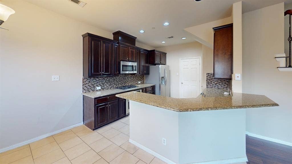 4651 Penelope Lane, Plano, TX 75024 Kitchen featuring dark wood cabinetry, granite countertops, tile backsplash, and stainless steel appliances