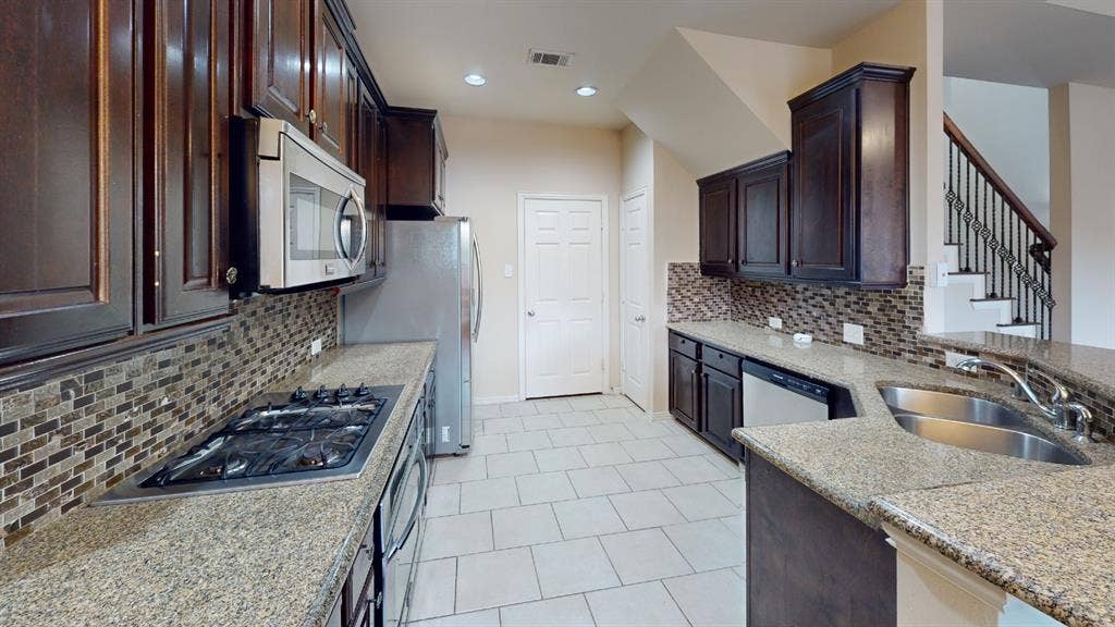 4651 Penelope Lane, Plano, TX 75024 Kitchen featuring dark wood cabinetry, granite countertops, mosaic tile backsplash, stainless steel appliances, and tile flooring