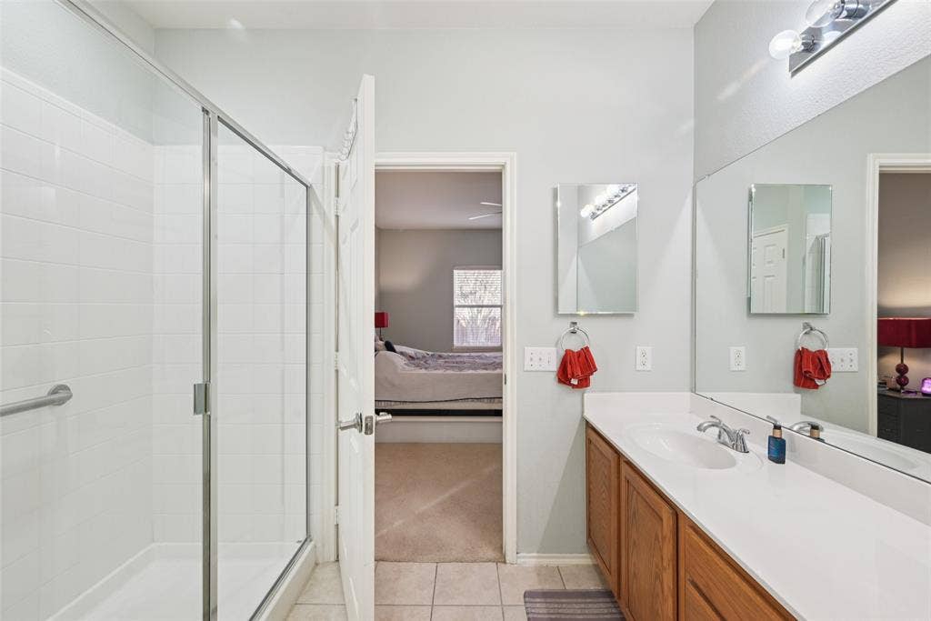 Walk-in shower with glass enclosure, single vanity with wood-finish cabinetry, integrated sink, and large mirror