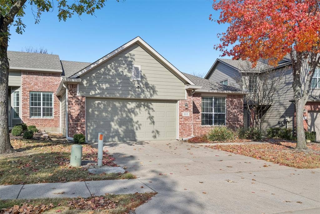 Brick and siding exterior with an attached garage, featuring a concrete driveway and mature trees