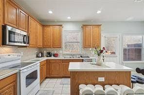 Kitchen with wood cabinetry, white tile flooring, white countertops, stainless steel microwave, and recessed lighting