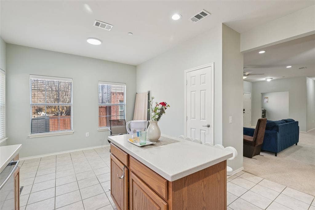 Kitchen island with wood-finish cabinetry and light-toned countertop, tile flooring, and recessed lighting