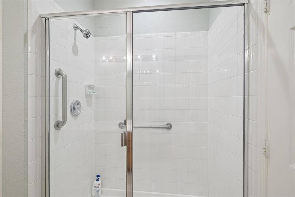 Shower stall with white subway tile, a chrome shower head, chrome shower controls, a built-in soap dish, and clear glass sliding doors