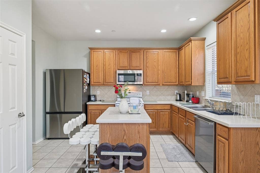 Kitchen with wood cabinetry, light-colored countertops, stainless steel appliances, and tiled flooring