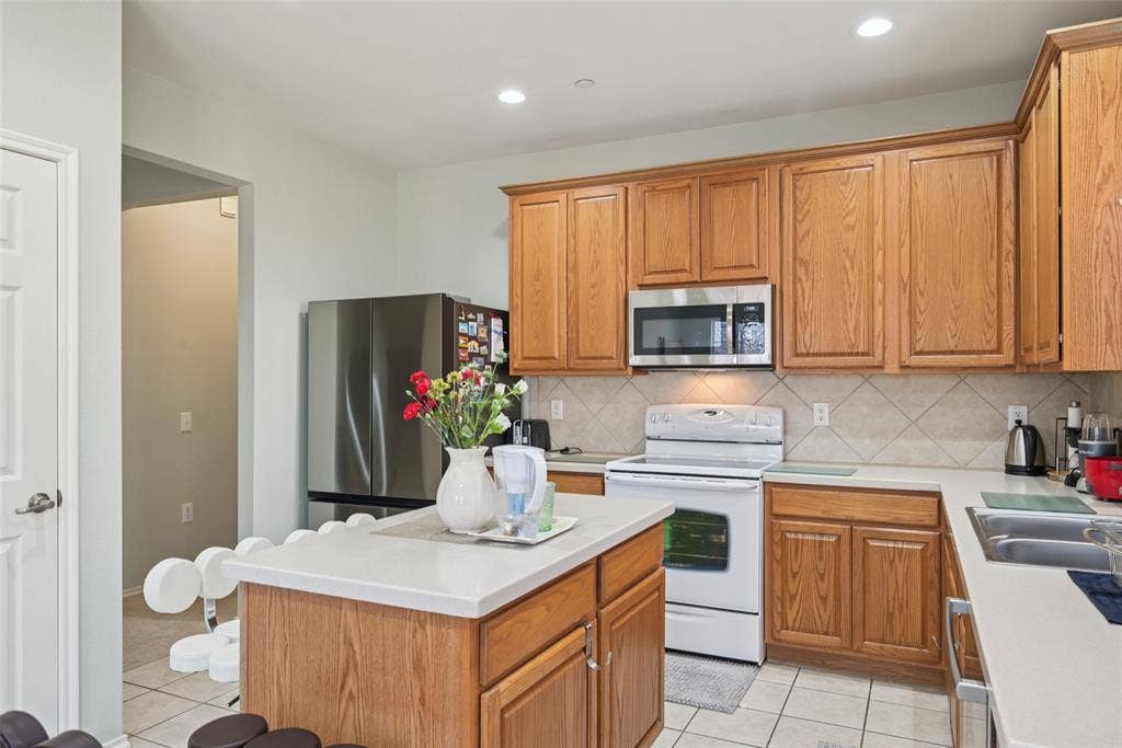 Kitchen featuring wood-finish cabinetry, tile backsplash, stainless steel appliances, and a central island with a light-toned countertop