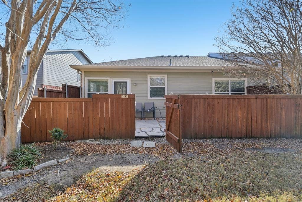 Rear exterior with light-colored siding, multiple windows, a private wood fence, and a stone patio