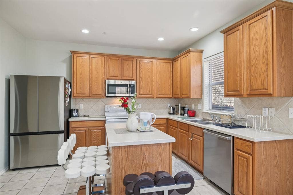 Kitchen featuring light-tone wood cabinetry, light-colored countertops, stainless steel appliances, and tiled flooring