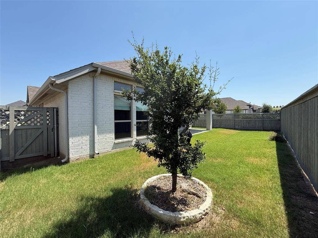 2401 Robin Way, Northlake, TX 76247 Expansive backyard featuring a manicured lawn, established tree with stone border, full privacy fencing, and a side access gate