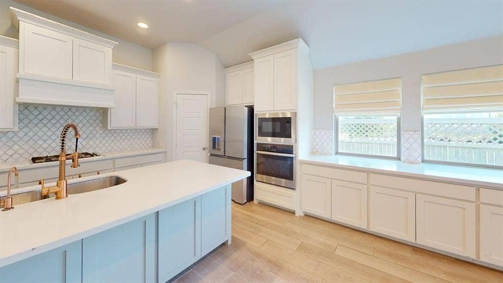 2401 Robin Way, Northlake, TX 76247 Kitchen featuring a large island with sink, white shaker-style cabinetry, light countertops, wood-finish flooring, and stainless steel appliances