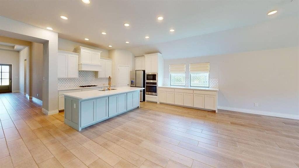 2401 Robin Way, Northlake, TX 76247 Open-concept kitchen featuring an expansive center island, integrated stainless steel appliances, a tile backsplash, and light wood-finish flooring