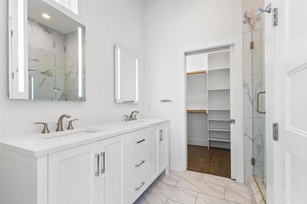 2450 N Garrett Avenue, #14, Dallas, TX 75206 Dual white vanities with integrated sinks, illuminated mirrors, tiled flooring, and a walk-in closet with built-in shelving