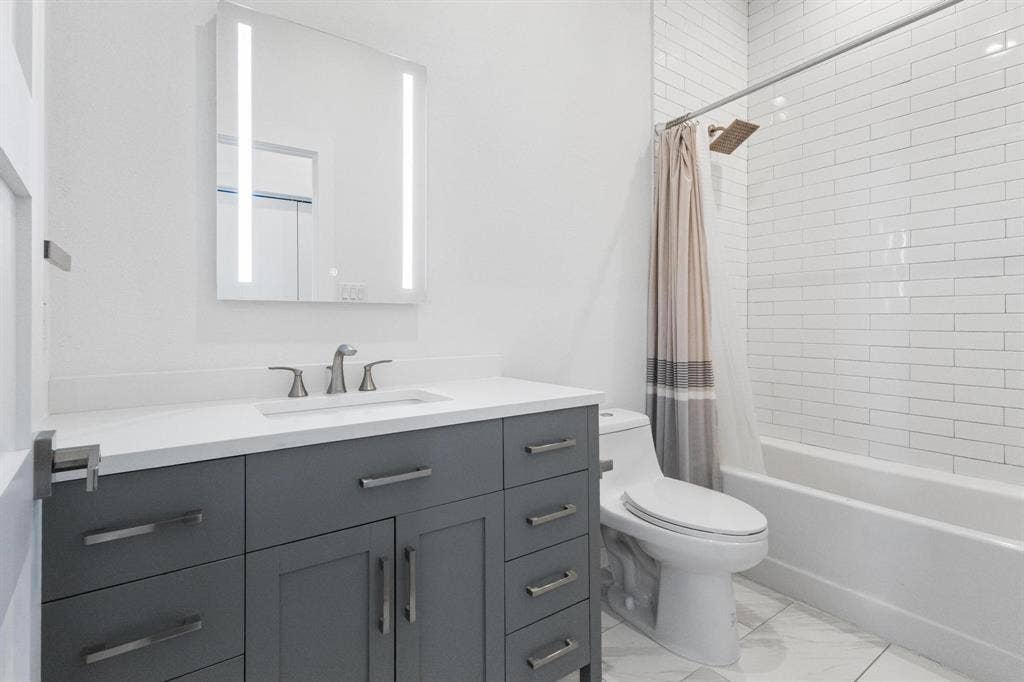 2450 N Garrett Avenue, #14, Dallas, TX 75206 White subway tile tub surround, sleek vanity with a quartz countertop, integrated rectangular sink, illuminated mirrored medicine cabinet, and contemporary floor tiling