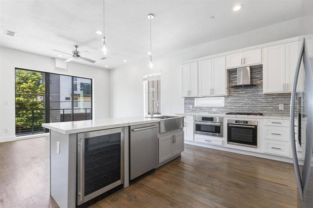 2450 N Garrett Avenue, #14, Dallas, TX 75206 Open-concept kitchen with wood-finish flooring, white cabinetry, stainless steel appliances, and a central island featuring a beverage cooler and farm sink