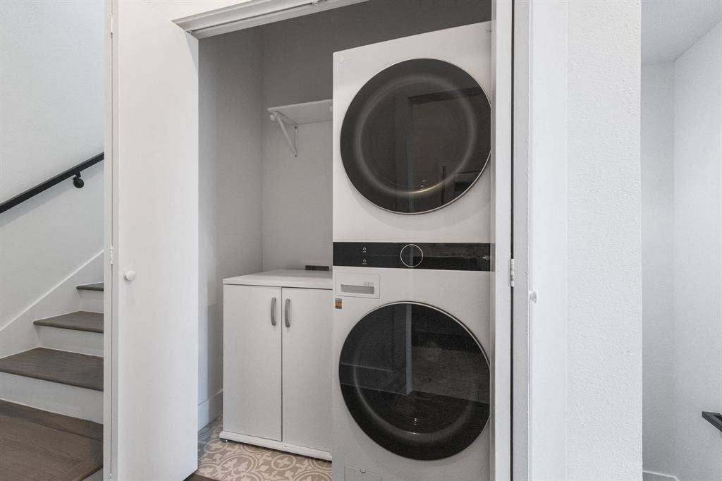 2450 N Garrett Avenue, #14, Dallas, TX 75206 Built-in stackable washer and dryer, adjacent storage cabinet, patterned floor tile, and wall-mounted shelving