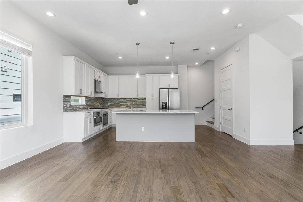 2450 N Garrett Avenue, #14, Dallas, TX 75206 Open-concept kitchen with white cabinetry and a central island, stainless steel appliances, mosaic tile backsplash, wood-finish flooring, and recessed lighting