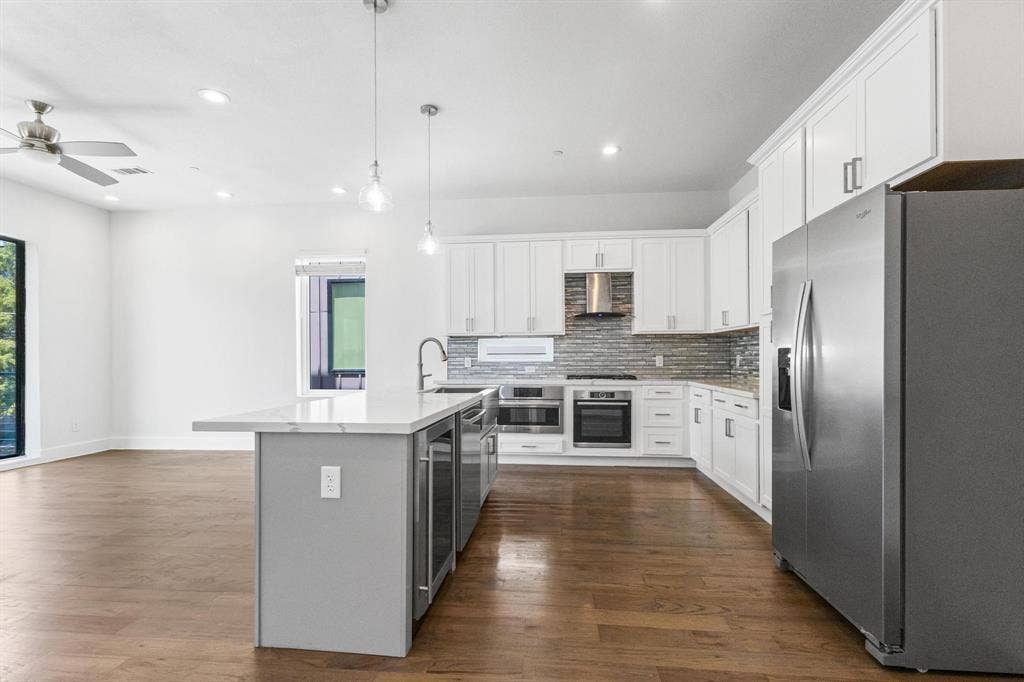 2450 N Garrett Avenue, #14, Dallas, TX 75206 Open-concept kitchen with white shaker cabinetry, stainless steel appliances, a tile backsplash, and an island featuring integrated beverage coolers