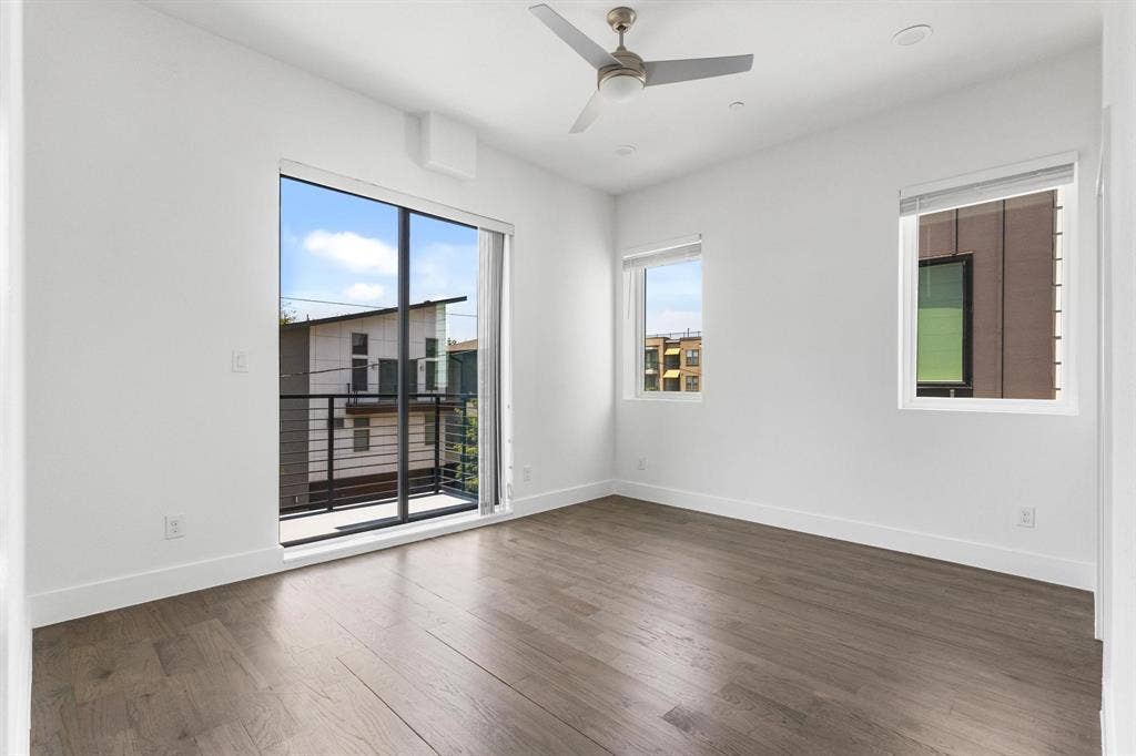 2450 N Garrett Avenue, #14, Dallas, TX 75206 Room featuring wood-finish flooring, a ceiling fan, multiple windows, and a sliding glass door opening to a balcony with metal railing