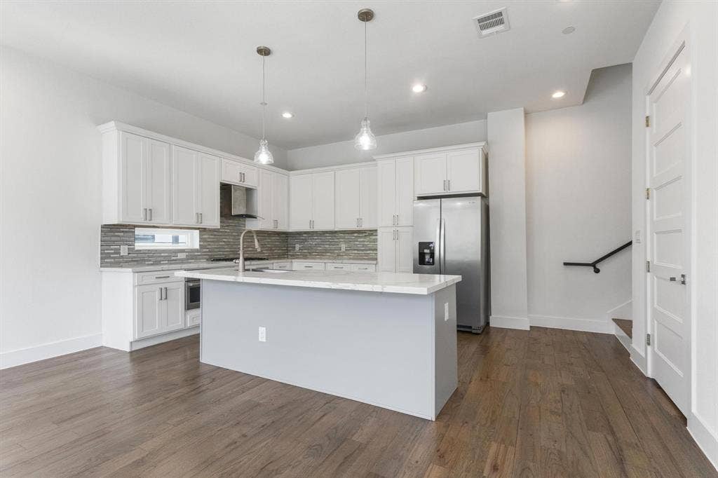 2450 N Garrett Avenue, #14, Dallas, TX 75206 Kitchen featuring white cabinetry, a large center island with a light-toned countertop, stainless steel appliances, a tiled backsplash, and wood-finish flooring