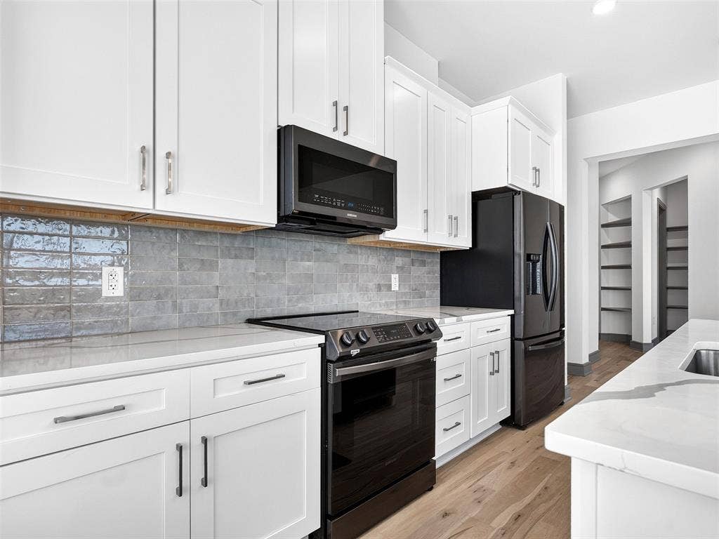 2700 Old Denton Road, #2212, Carrollton, TX 75007 White shaker cabinetry, black stainless steel appliances, stone countertops, gray subway tile backsplash, and wood-finish flooring