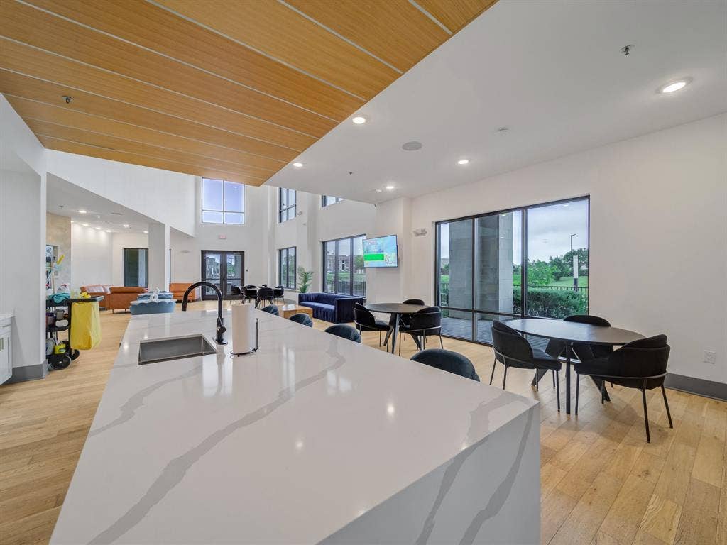 2700 Old Denton Road, #2212, Carrollton, TX 75007 Expansive common area featuring a waterfall island with an undermount sink, wood-finish flooring, a wood-slat ceiling accent, and large windows