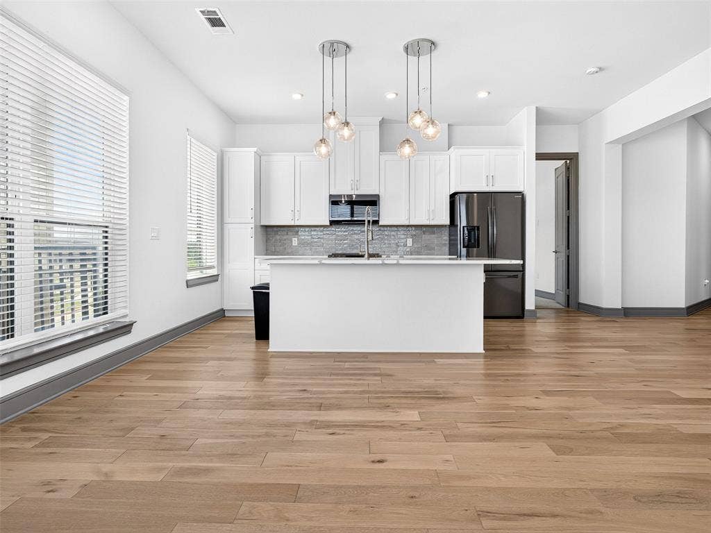 2700 Old Denton Road, #2212, Carrollton, TX 75007 Kitchen featuring white cabinetry, a central island, stainless steel appliances, wood-finish flooring, and pendant lighting