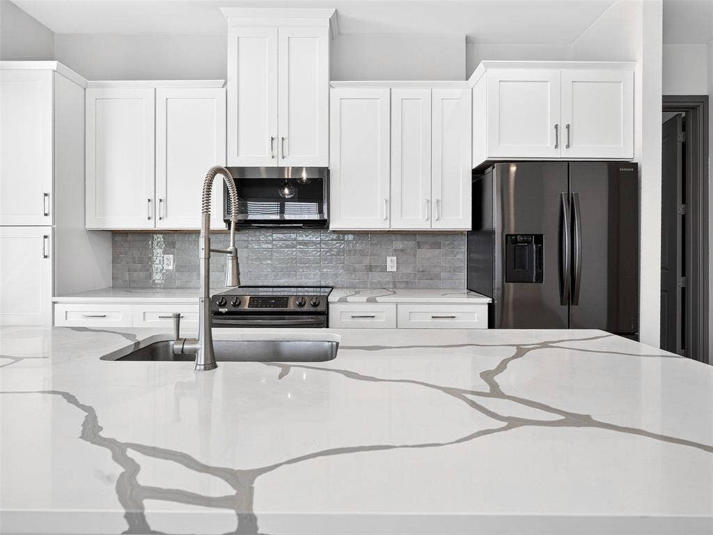 2700 Old Denton Road, #2212, Carrollton, TX 75007 Kitchen featuring white shaker-style cabinetry, a large kitchen island with a white countertop and gray veining, stainless steel sink with a high-arc faucet, and dark gray appliances