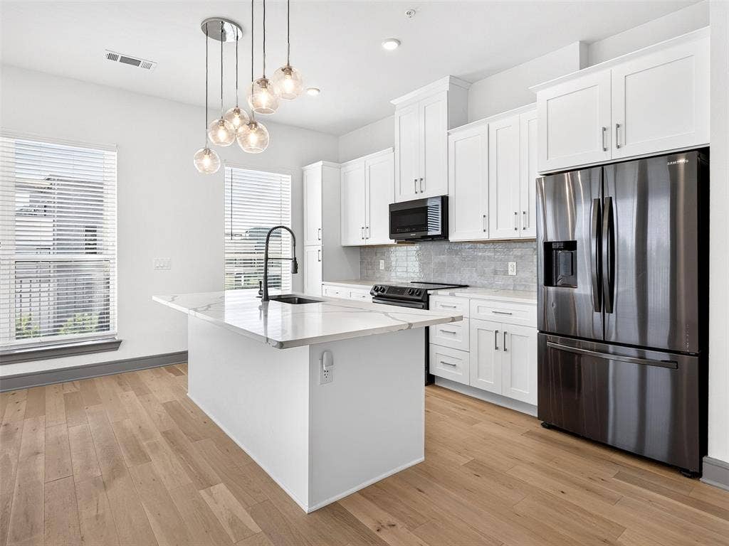 2700 Old Denton Road, #2212, Carrollton, TX 75007 Kitchen featuring a central island with a sink, stainless steel appliances, white cabinetry, wood-finish flooring, and pendant lighting