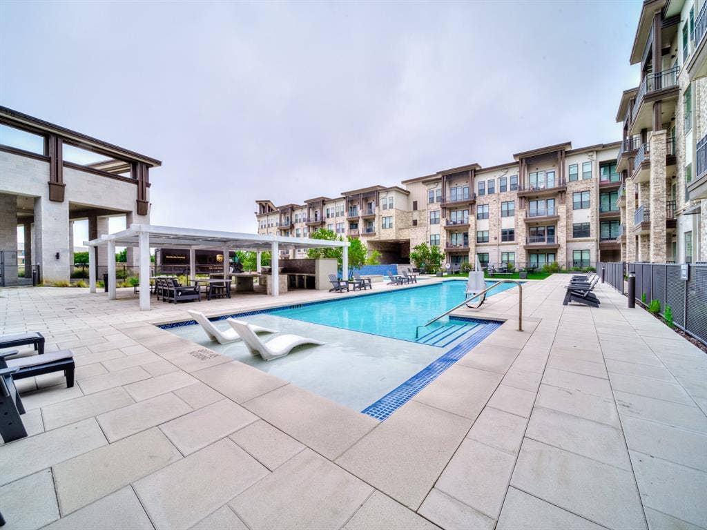 2700 Old Denton Road, #2212, Carrollton, TX 75007 Expansive outdoor pool area featuring a rectangular pool, integrated lounge seating, and a shaded pergola with built-in grilling stations