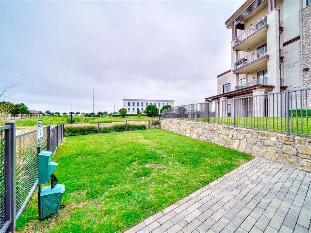 2700 Old Denton Road, #2212, Carrollton, TX 75007 Manicured green space with a paver walkway, stone retaining wall, and metal fencing